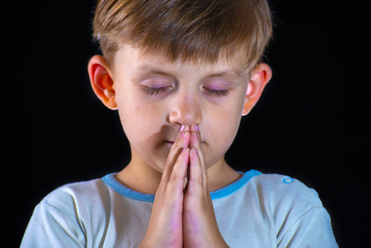 The little boy prays to God with his hands bent. Close-up on a black background