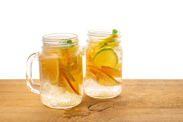 jars of homemade lemonade with sliced fresh lemon, orange, lime, twig mint and bubbles on wooden background isolated, detox fruit infused water