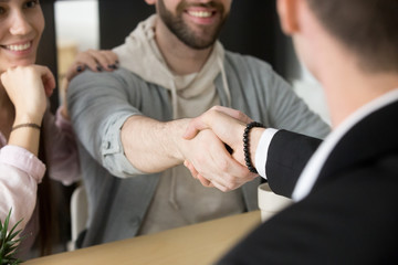 Close up of satisfied couple shaking hand of realtor or broker, closing purchase deal on buying...