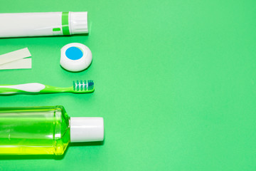 Dental care tools: toothpaste, toothbrush, dental floss, gum and mouthwash on green background