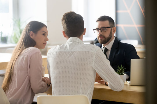 Serious Broker Or Realtor Listening To Millennial Couple Arguments Or Ideas During Office Meeting, Insurance Agent Consulting Clients On House Purchase, Becoming Property Owners Or Taking Loan.