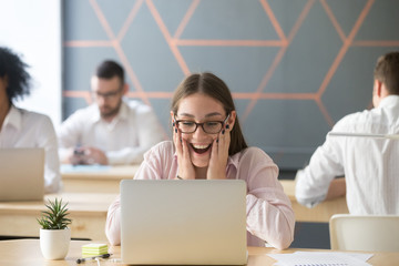 Happy female employee excited seeing promotion email or message at laptop in coworking office, satisfied student get exam results, amazed by high grades, worker rewarded for great achievements