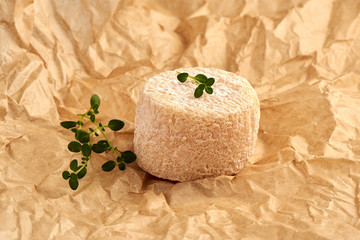 Crottin cheese with thyme leaves on brown package paper.
