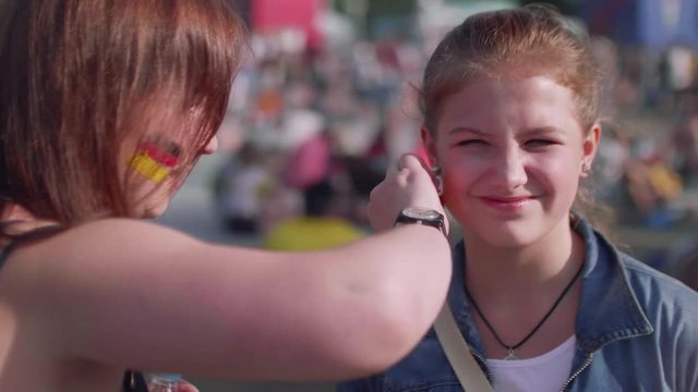 Girl wipes cheeck of other girl in fan zone.