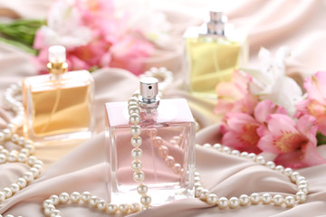 Fototapeta na wymiar Perfume bottles with flowers and beads on satin background