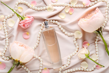 Perfume bottle with flowers and beads on satin background