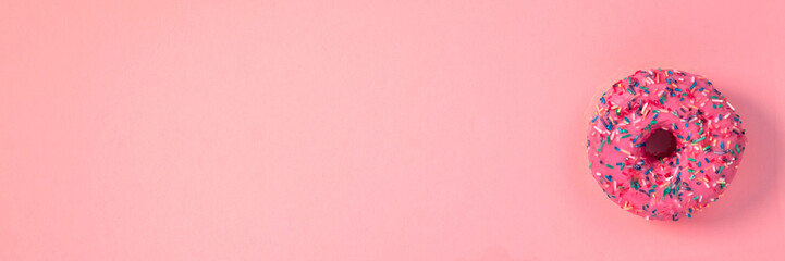 Panoramic view on pink donut with colorful sprinkles on an empty pink pastel background