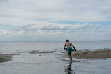 Fototapeta premium a young man goes in for water sports with skimboarding in shallow water on the shore
