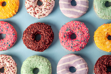 Many colorful donuts with sprinkles and icing on a blue pastel background