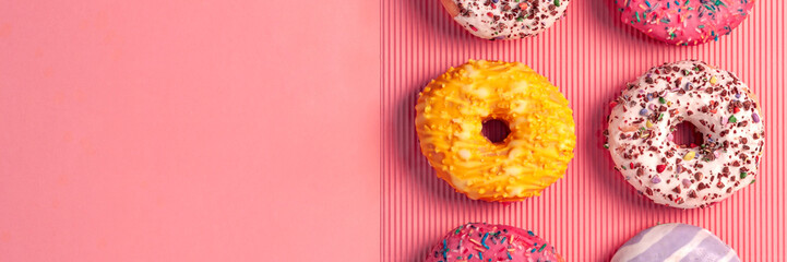 Panoramic view on six colorful donuts with sprinkles and icing on an empty powder pink background
