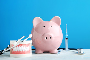 Pink piggy bank with stethoscope, syringe and teeth model on blue background