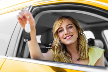 An attractive woman in the yellow car holds a car key in her hand.