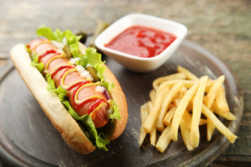 Hot dog with vegetables and french fries on wooden table
