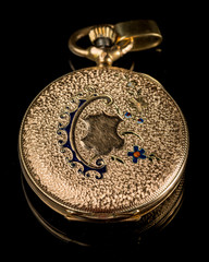 Old golden pocket watch on a black reflective surface