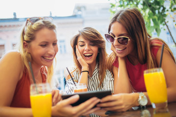 Three beautiful friends in a cafe using tablet pc and having fun