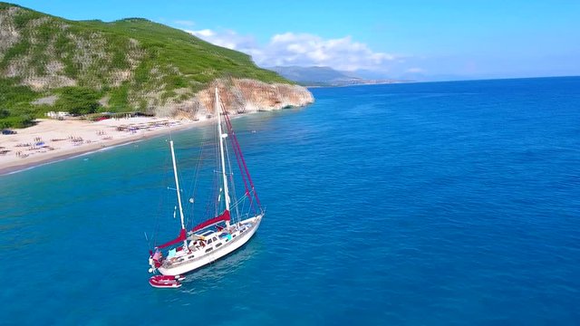 Summer Ionian Sea Aerial with white Yacht. coastline view with sandy beach on the sunset with green bushes Albania dhermi gjipe beach. Boat near beach.