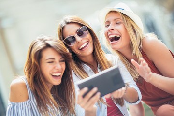 Three happy smiling female friends sharing a tablet computer as they stand close together looking at the screen