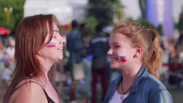 Girls happily hug and dance in fan zone during football match