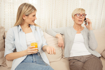 Young woman is curious and anticipating good news from her mother who is talking on the phone. Happy family moments at home