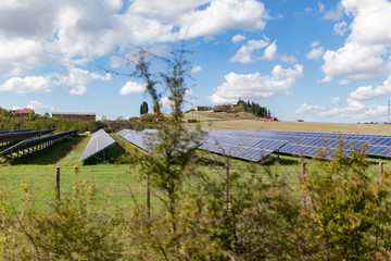 Solar panels in a field in Italy on a bright day with blue sky and clouds