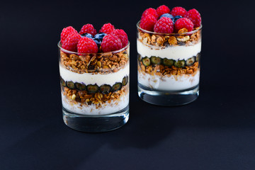 Healthy blueberry and raspberry parfait in a glass on a black background. Two portions. Space for text or design.
