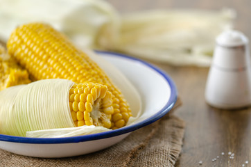 Cooked corncobs in white dish on rustic napkin.