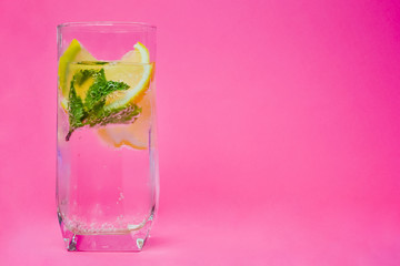 Glass of water, lemon and mint on pink background.
