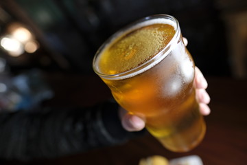 Hand holding a Glass with golden beer horizontal close up  in a black background focus foam crystal cold summer ice alcohol beverage bar liquid lemon refreshment brown cocktail tea drink