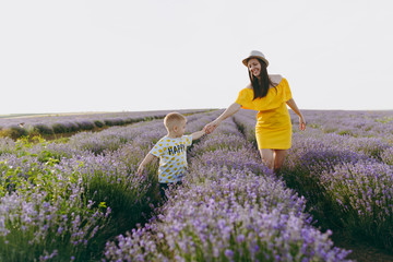 Obraz premium Young woman in yellow dress walk on purple lavender flower meadow field background, rest, have fun, play with little cute child baby boy. Mother, small kid son. Family day, parents, children concept.