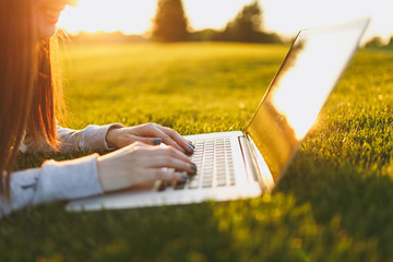 Close up hands on keyboard. Woman working on laptop pc computer with blank black empty screen to copy space in park on green grass sunshine lawn outdoors. Mobile Office. Freelance business concept.