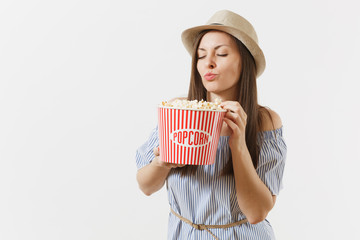 Young woman in blue dress, hat watching movie film holding eating popcorn from bucket isolated on white background. People, sincere emotions in cinema, lifestyle concept. Advertising area. Copy space.