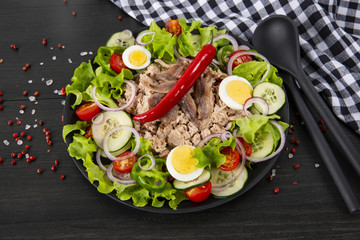 Salad with tuna, anchovies and vegetables. Mediterranean food. The background is black. Top view. Copy space. Horizontal shot.