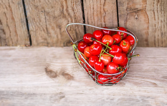 Cherry in small metal basket on wooden surface. Fresh ripe organic berries.