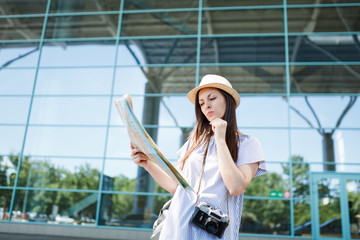 Young concerned traveler tourist woman with retro vintage photo camera looking in paper map, search route at international airport. Passenger traveling abroad on weekends getaway. Air flight concept.