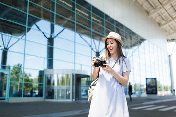 Young surprised traveler tourist woman with backpack looking on retro vintage photo camera at international airport. Female passenger traveling abroad to travel on weekend getaway. Air flight concept.