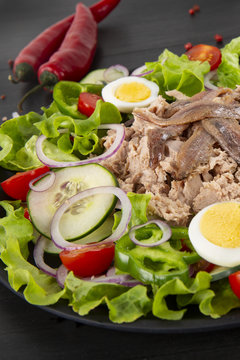 Salad with tuna, anchovies and vegetables. Mediterranean food. The background is black. Top view. Copy space. .