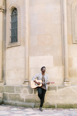 Portrait of young african man playing guitar for tourists sitting on the fountain in the city