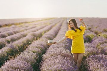 Portrait of young sensual beautiful woman in yellow dress, hat on purple lavender flower blossom meadow field outdoors on summer nature background. Tender female near flowering bush. Lifestyle concept