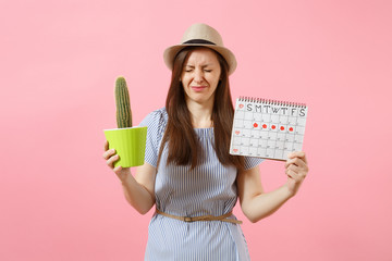 Sad sickness woman in blue dress holding green cactus, periods calendar for checking menstruation days isolated on pink background. Medical, healthcare, gynecological, tummy pain concept. Copy space.