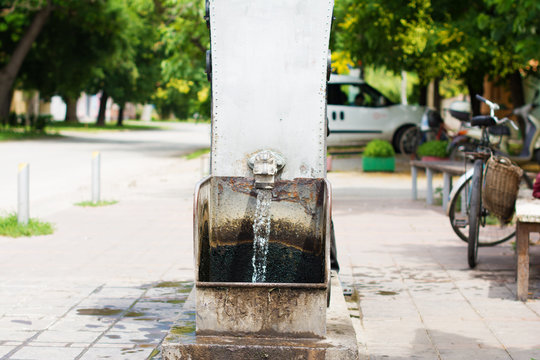 Flowing artesian well, and a decorative spigot installed on it. Selective focus. The blurry contours of a vintage bicycle with a wicker bag is visible in the nearest surroundings.