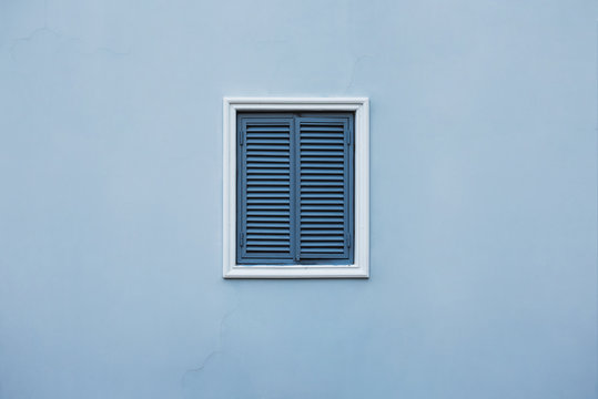 Blue wall of the house with a closed window and details.