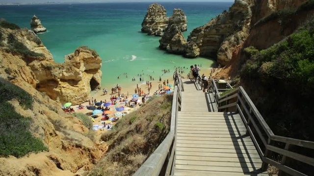 Panoramic wooden walkway footbridge to scenic Praia do Camilo in Lagos coast, Algarve, Portugal. Perspective view downward of the long stairs to turquoise waters of Algarve. Summer holidays in Europe.