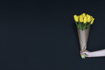 Spring yellow tulips. Woman holding a bouquet on black background. Flat lay, top view. Tulip flower background. Add your text.