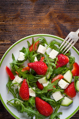 Fresh vegetable strawberry salad on white plate on natural rustic desk.