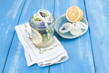 Traditional Dutch marinated herring with lemon and onions in a jar. Seafood on a blue background....
