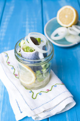 Traditional Dutch marinated herring with lemon and onions in a jar. Seafood on a blue background. Copy space.