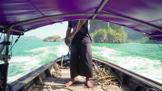 Unrecognizable man drives a long-tail thai boat with outboard motor 4K