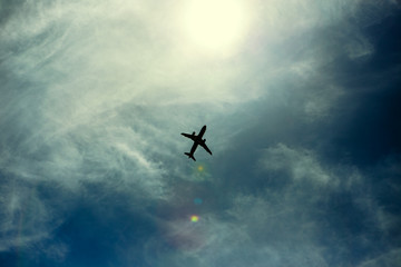 A silhouette of a plane flying overhead on a clear day.