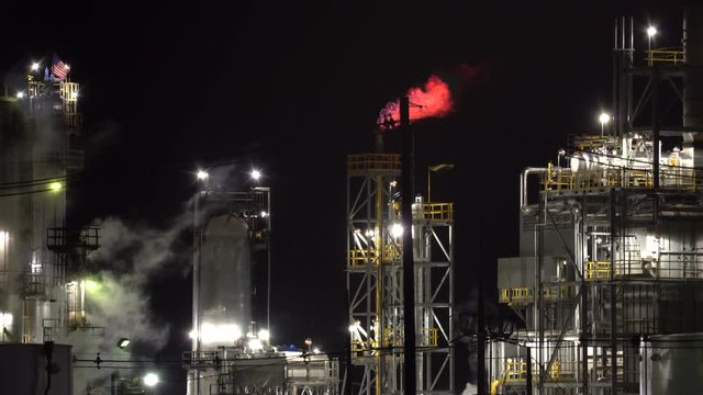 Smoking oil refinery plant with flame at night - United States