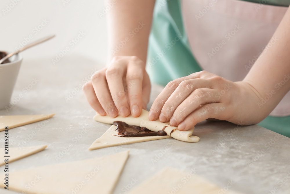 Wall mural woman preparing tasty croissants with chocolate paste on table, closeup